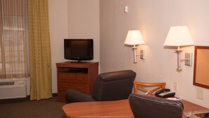 Hotelkamer met een televisie op een houten standaard, een bureau met stoel, twee wandlampen en een telefoon.