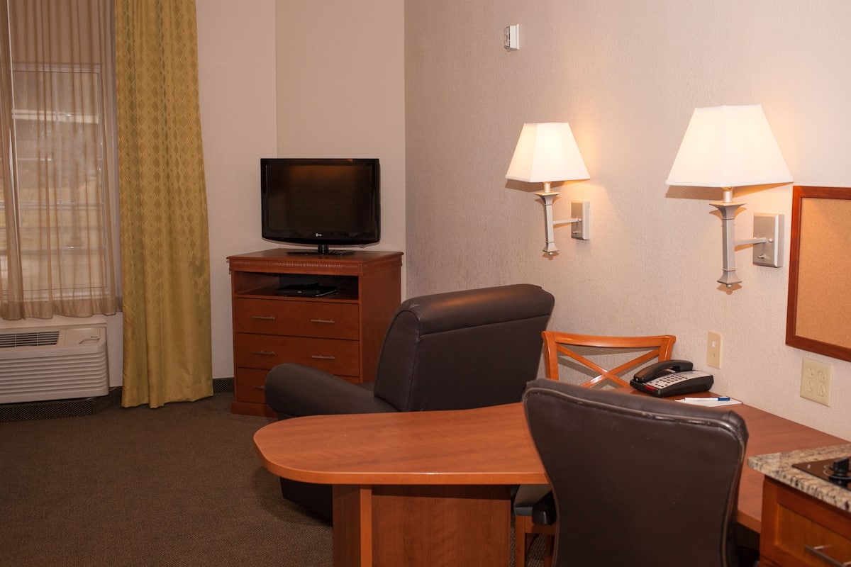 A hotel room with a television on a wooden stand, a desk with a chair, two wall-mounted lamps, and a telephone.