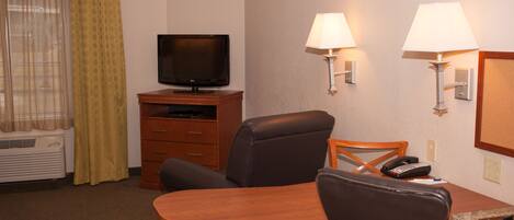 Una habitación de hotel con televisión sobre un soporte de madera, un escritorio con silla, dos lámparas de pared y un teléfono.
