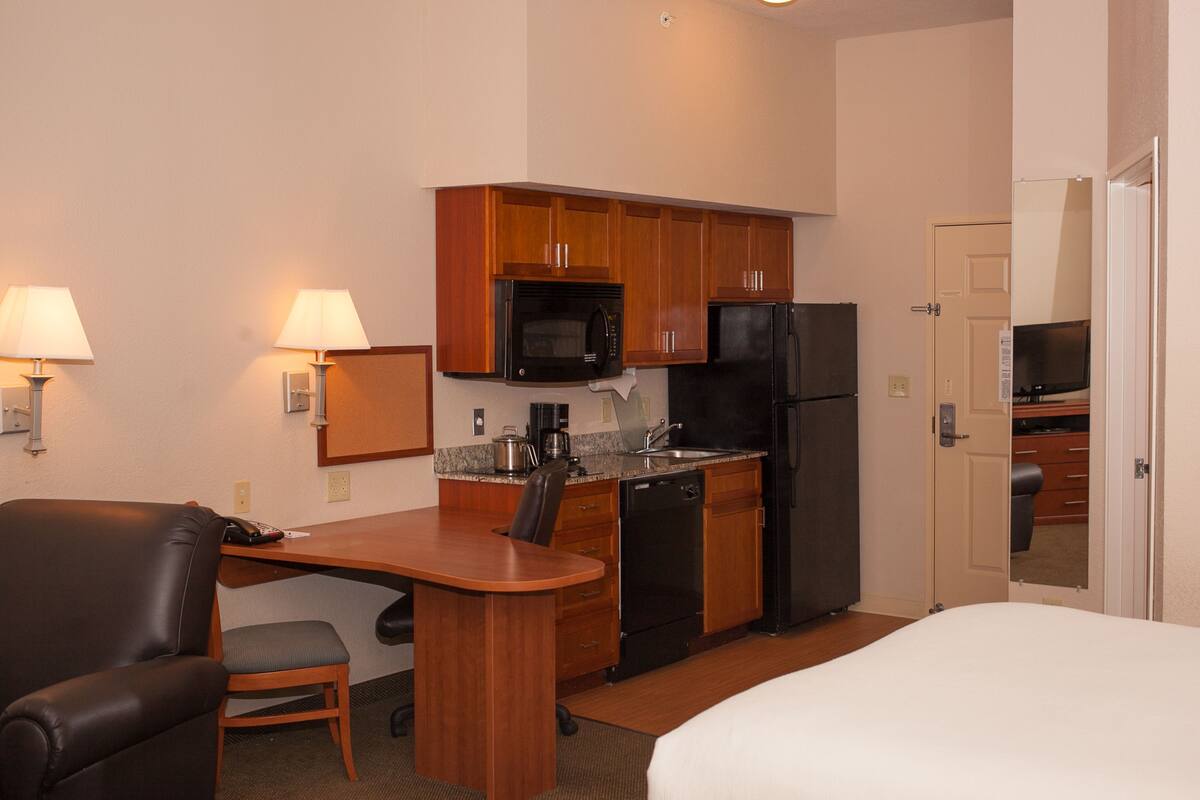 A hotel room with a kitchenette, a bed, a desk with a chair, and a TV.