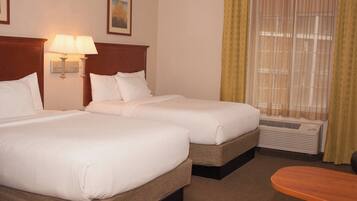 A hotel room with two beds, a nightstand with lamps, a window with curtains, and a wooden table.