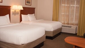 Een hotelkamer met twee bedden, een nachtkastje met lampen, een raam met gordijnen en een kleine tafel.