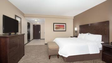 A hotel room with a large bed, a TV on a dresser, a mirror, a painting on the wall, and a patterned carpet.