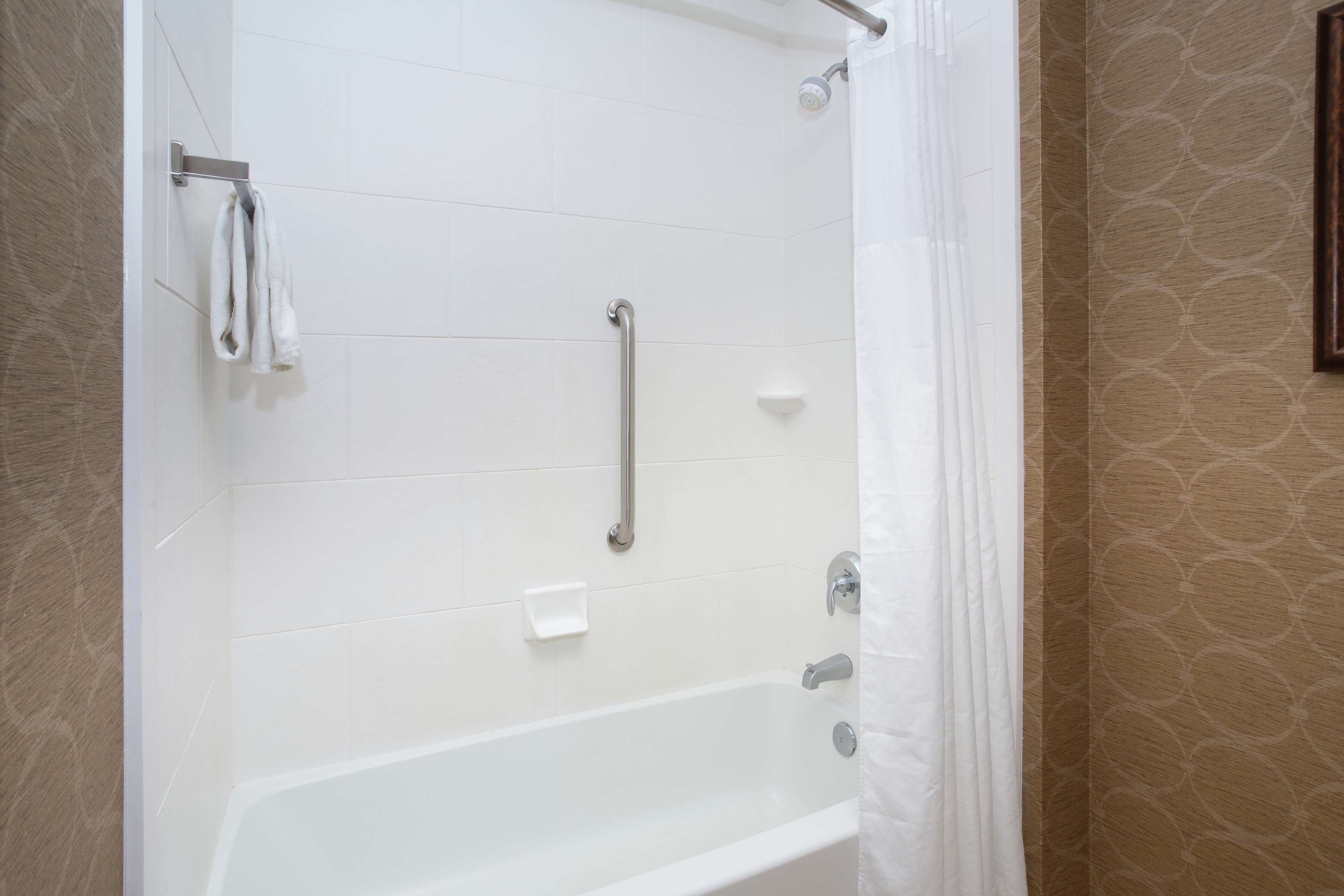 A bathroom with a white bathtub, a shower with a handheld showerhead, and a towel rack.