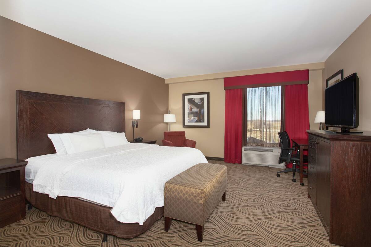 Ein Hotelzimmer mit einem großen Bett, einem Schreibtisch, einem Stuhl und einem Fernseher.