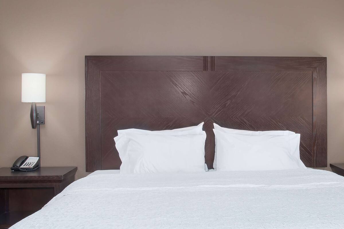 Ein Hotelzimmer mit einem großen Bett, einem Nachttisch mit Lampe und Telefon sowie einem Holzkopfteil.
