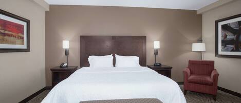 A hotel room with a large bed, two bedside tables with lamps, a red armchair, and a patterned carpet.
