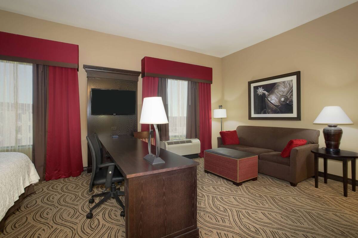 Ein Hotelzimmer mit Bett, Schreibtisch mit Stuhl, Sofa, Couchtisch, Fernseher und zwei Lampen.