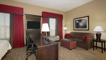 Ein Hotelzimmer mit Bett, Schreibtisch mit Stuhl, Sofa, Couchtisch, Fernseher und zwei Lampen.
