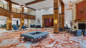 A spacious lobby with a high ceiling, wooden beams, a large seating area, and a fireplace.