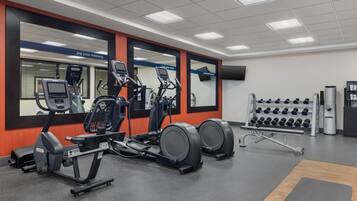 Une salle de sport équipée de machines de cardio, d’haltères et d’un mur recouvert de miroirs.