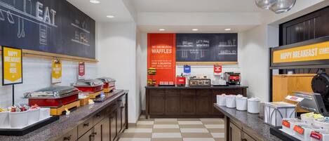 A breakfast area with a checkered floor, buffet counters, and signs advertising waffles and breakfast.