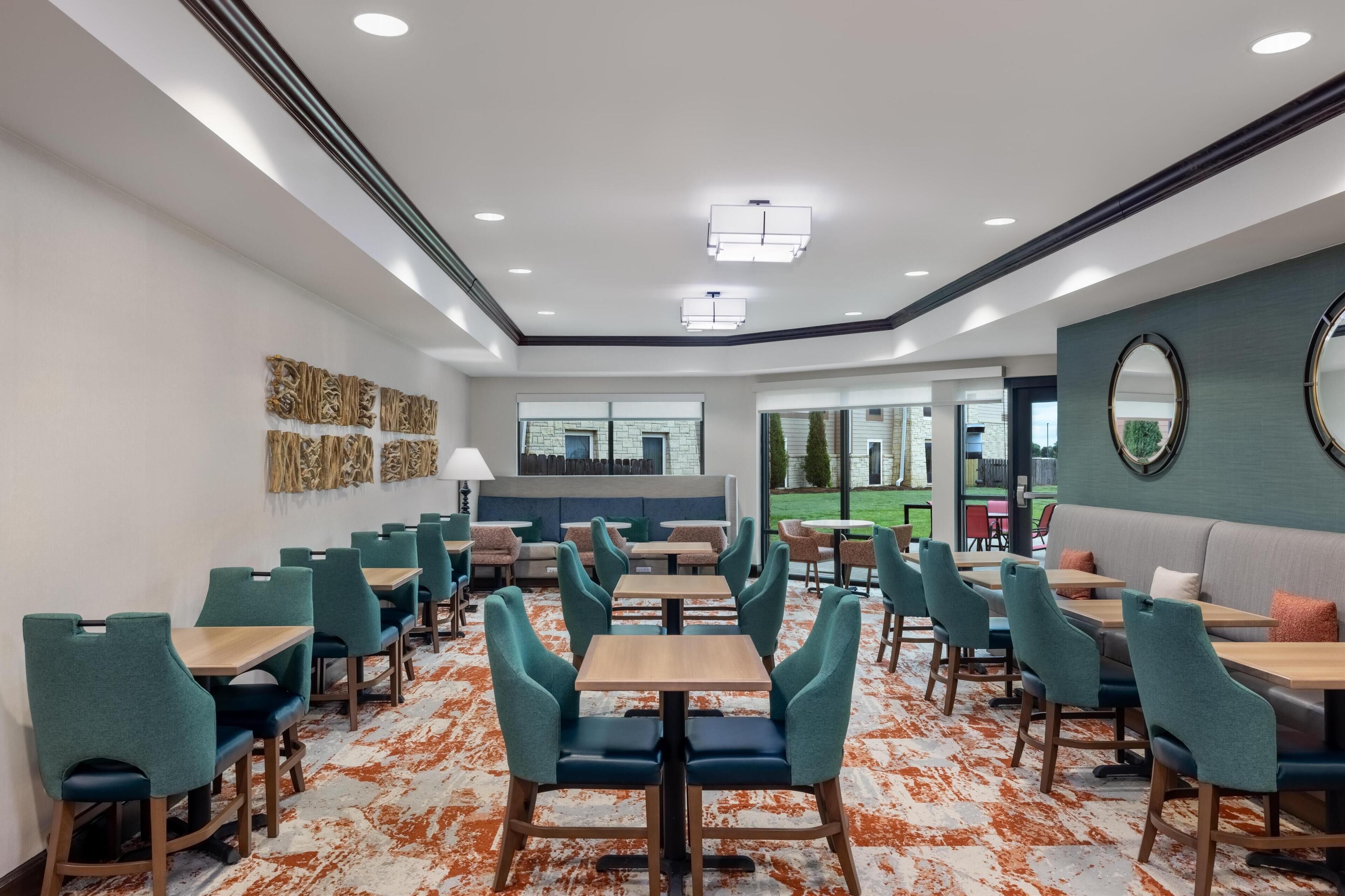 A modern dining area with rows of tables and chairs, a central seating area, and a view of the outdoors.