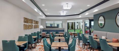 A modern dining area with rows of tables and chairs, a central seating area, and a view of the outdoors.