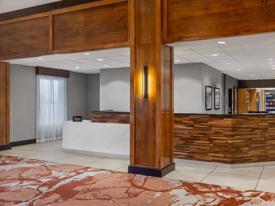 A hotel lobby with a reception desk, wooden paneling, a large pillar, and a tiled floor.