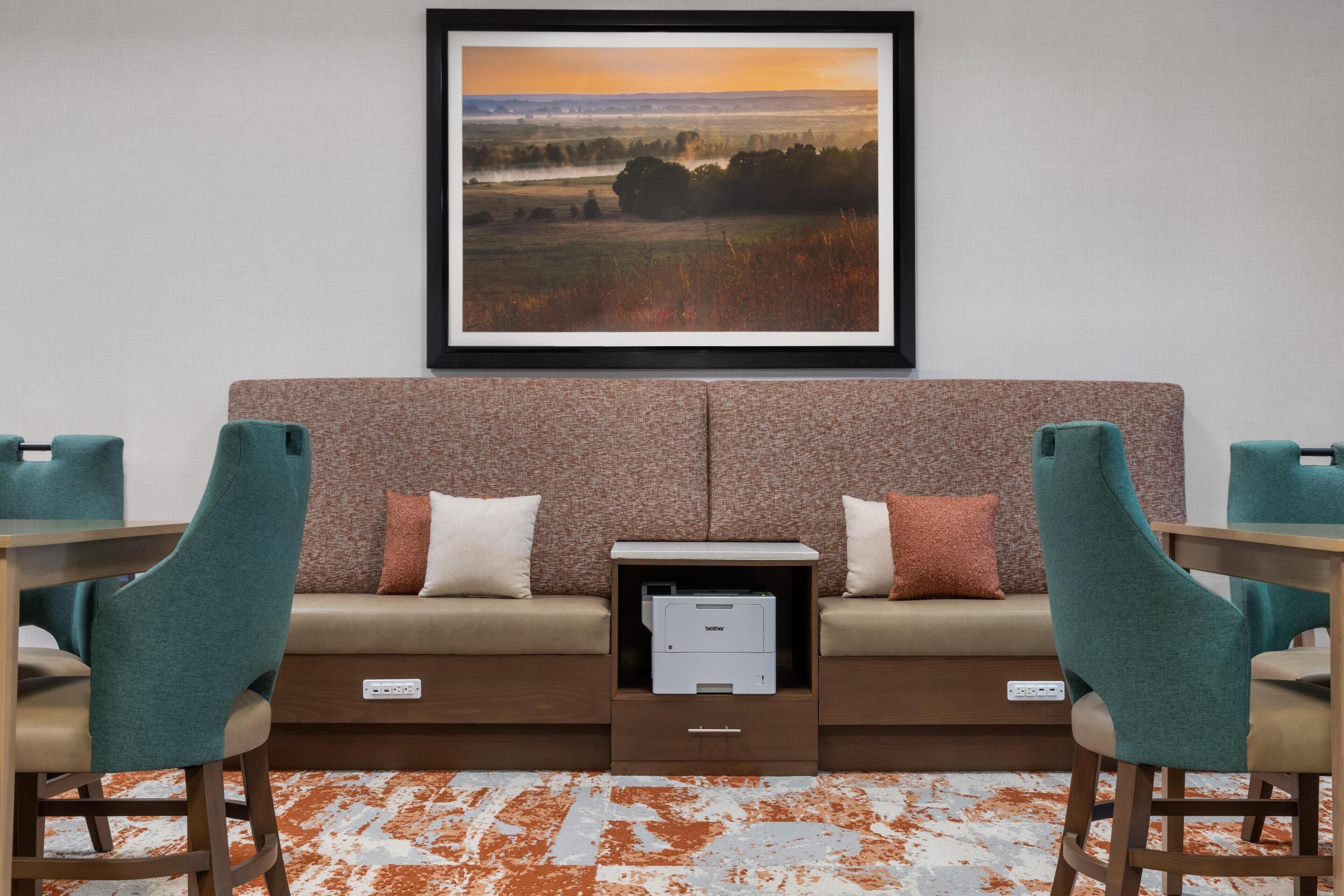 Un salon moderne avec un canapé, deux fauteuils turquoise, une table basse et un tableau représentant un paysage, encadré et placé au-dessus du canapé.