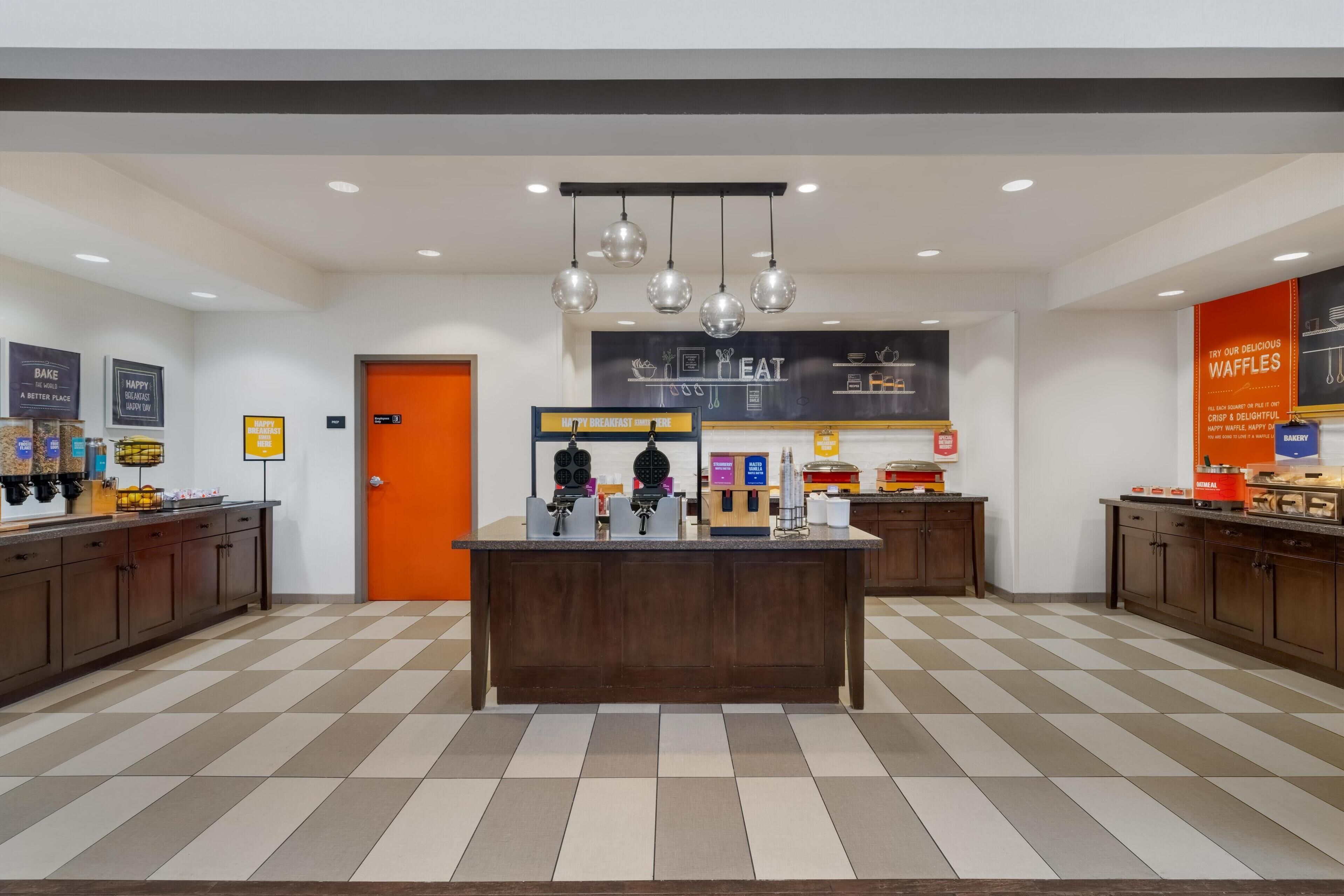 A modern kitchen area with a central island, overhead pendant lights, and a chalkboard menu.
