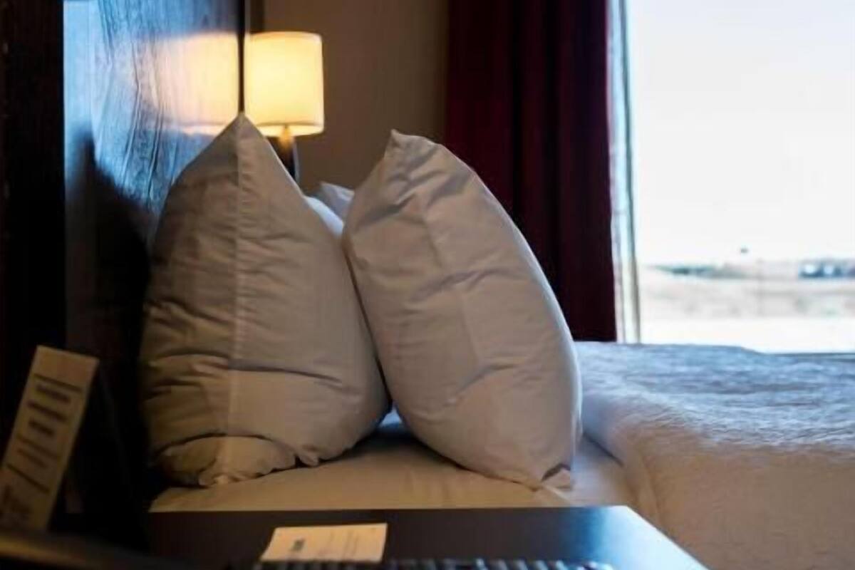 Une chambre d’hôtel avec un lit, des oreillers, une télécommande, une lampe et une fenêtre avec des rideaux.