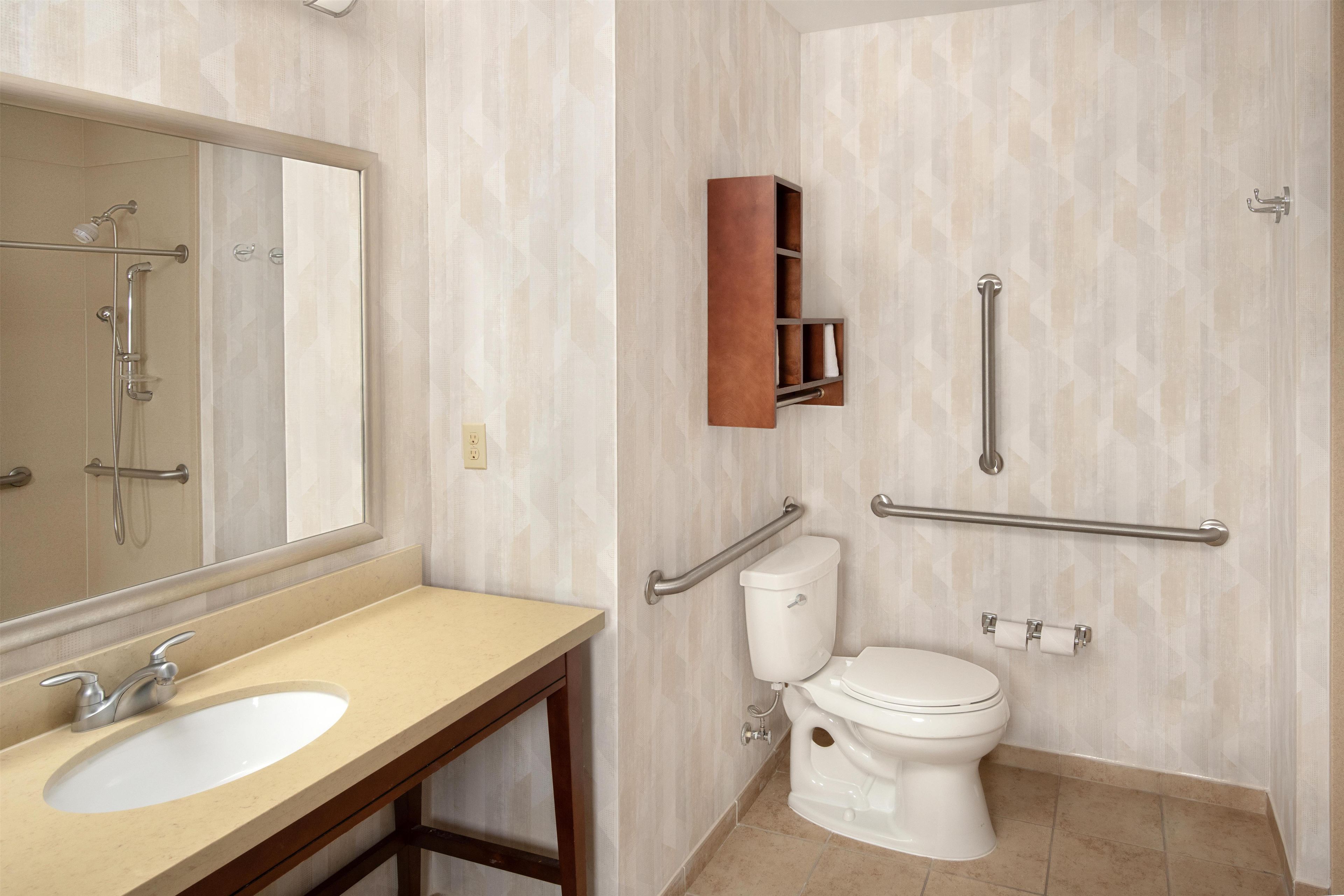 Un baño con lavamanos, espejo, inodoro y barras de apoyo.