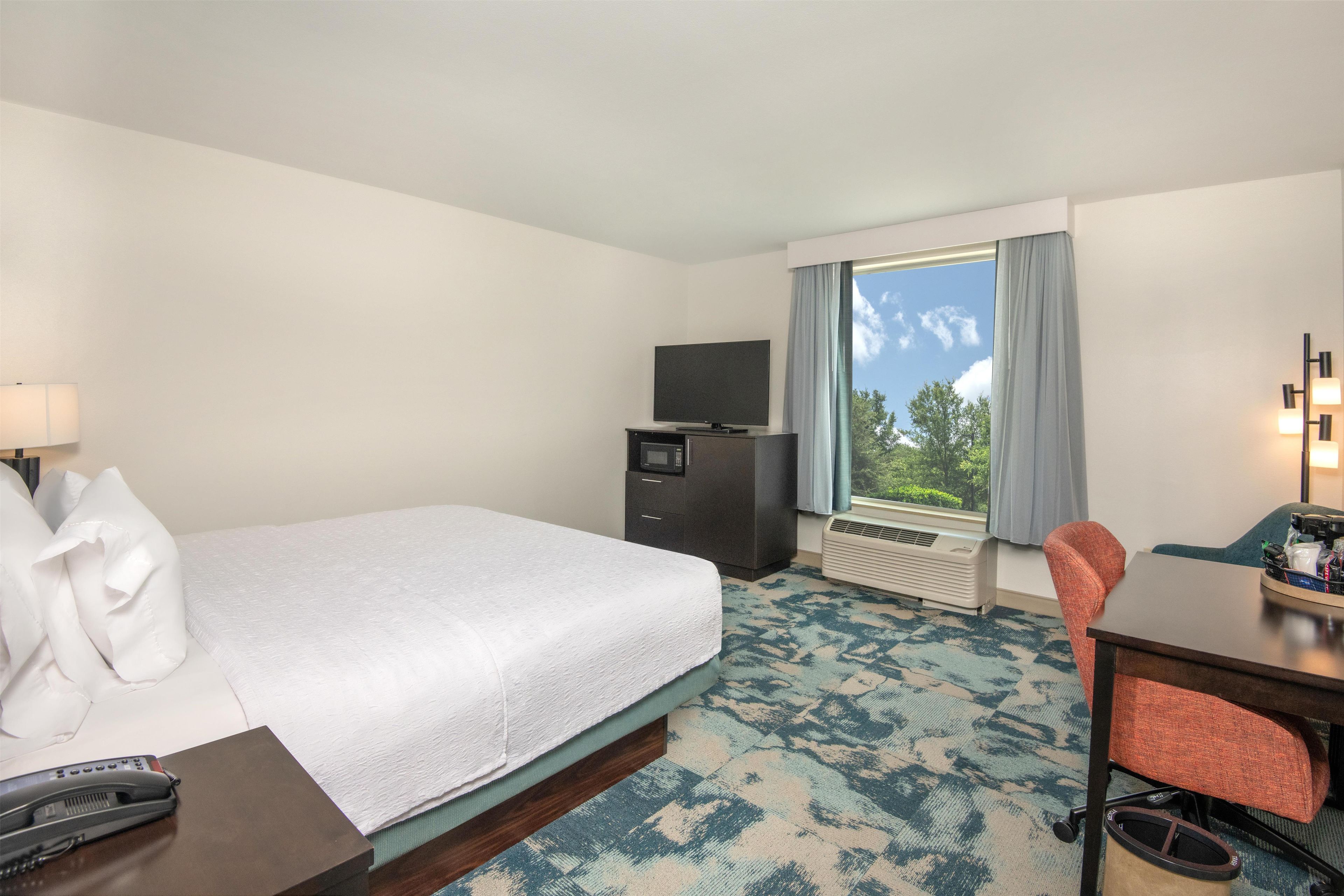 A hotel room with a bed, a desk, a chair, a television, and a window with curtains.