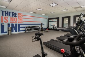 Un gimnasio con cintas de correr, mancuernas y una pared decorada con mensajes motivacionales.