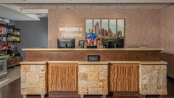 A hotel reception desk with a cityscape mural, a snack bar to the left, and a stone-textured counter.