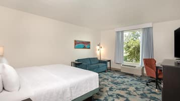 A hotel room with a bed, a desk, a chair, a lamp, and a painting on the wall.