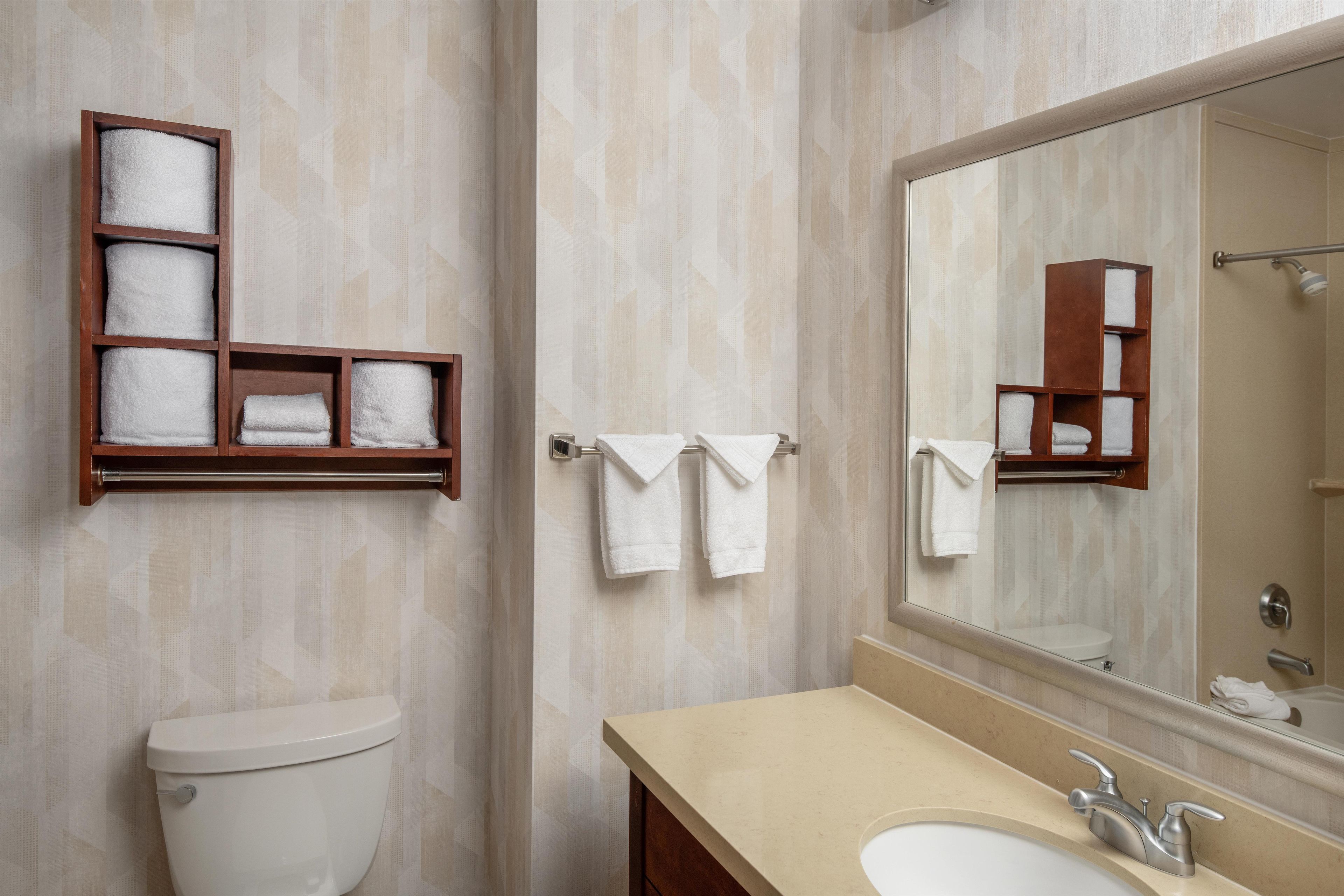 Un baño con inodoro, lavamanos, espejo y toallero con varias toallas.