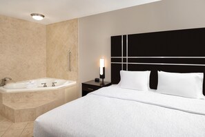Habitació d'hotel amb un llit gran, una banyera separada i una petita taula de nit amb una làmpada.
