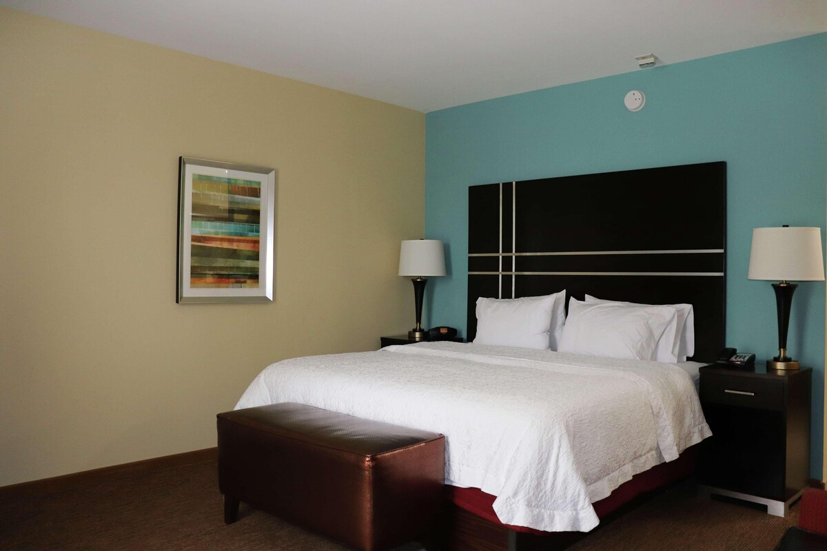 A hotel room with a large bed, a nightstand, a lamp, and a framed picture on the wall.