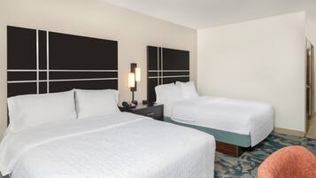 A hotel room with two beds, a nightstand with a lamp, and a chair.