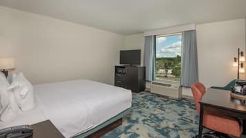 Quarto de hotel com cama, escrivaninha, cadeira, televisão e janela com cortinas.