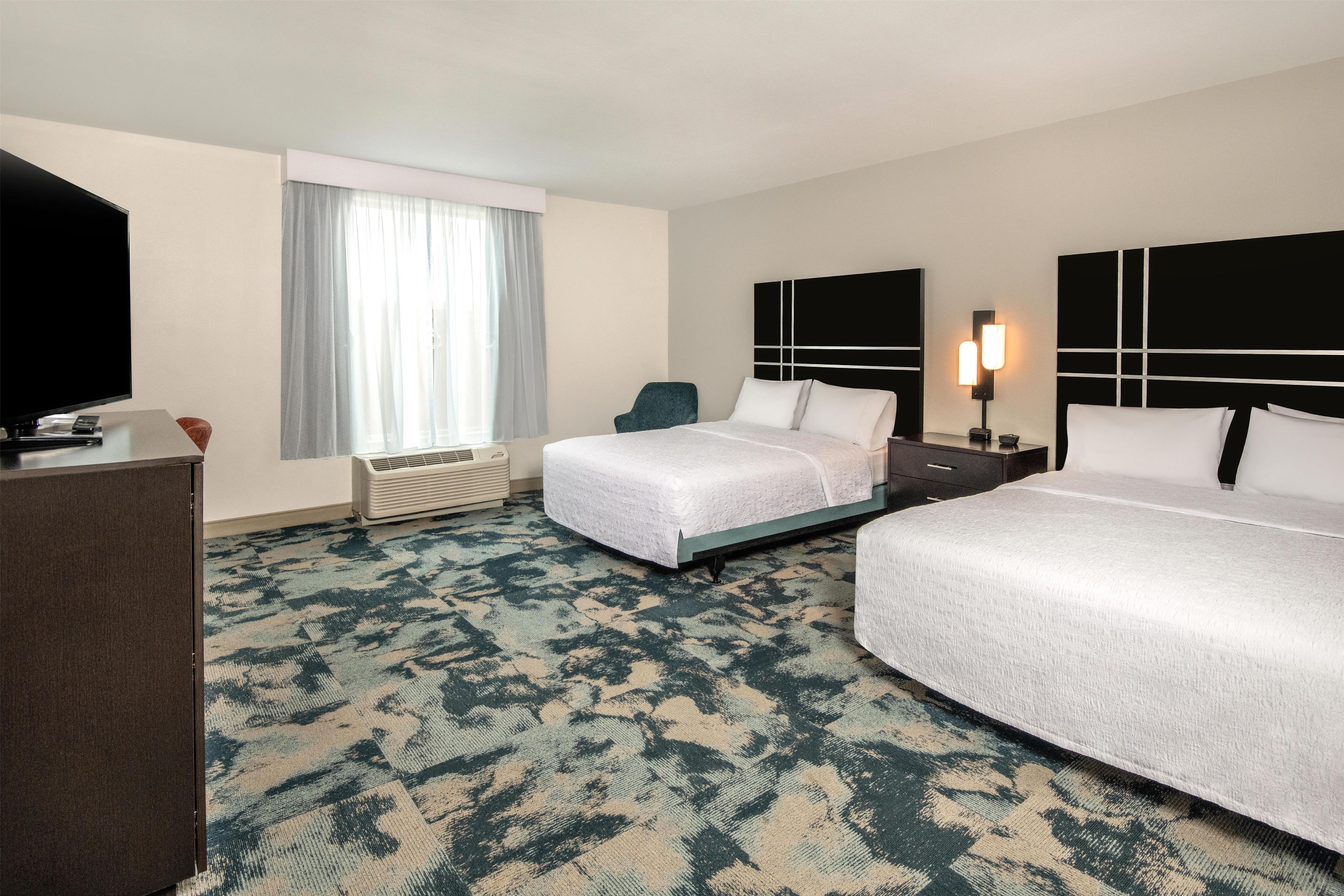 Habitación de hotel con dos camas, un escritorio, un televisor y una ventana con cortinas.