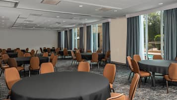 Un salón de conferencias con mesas y sillas redondas, ventanas amplias y vistas al exterior.