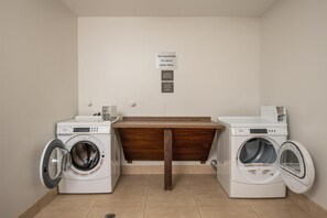 A laundry room with two Whirlpool washers and a wooden bench. - Hampton Inn Austin/Oak Hill (Austin)