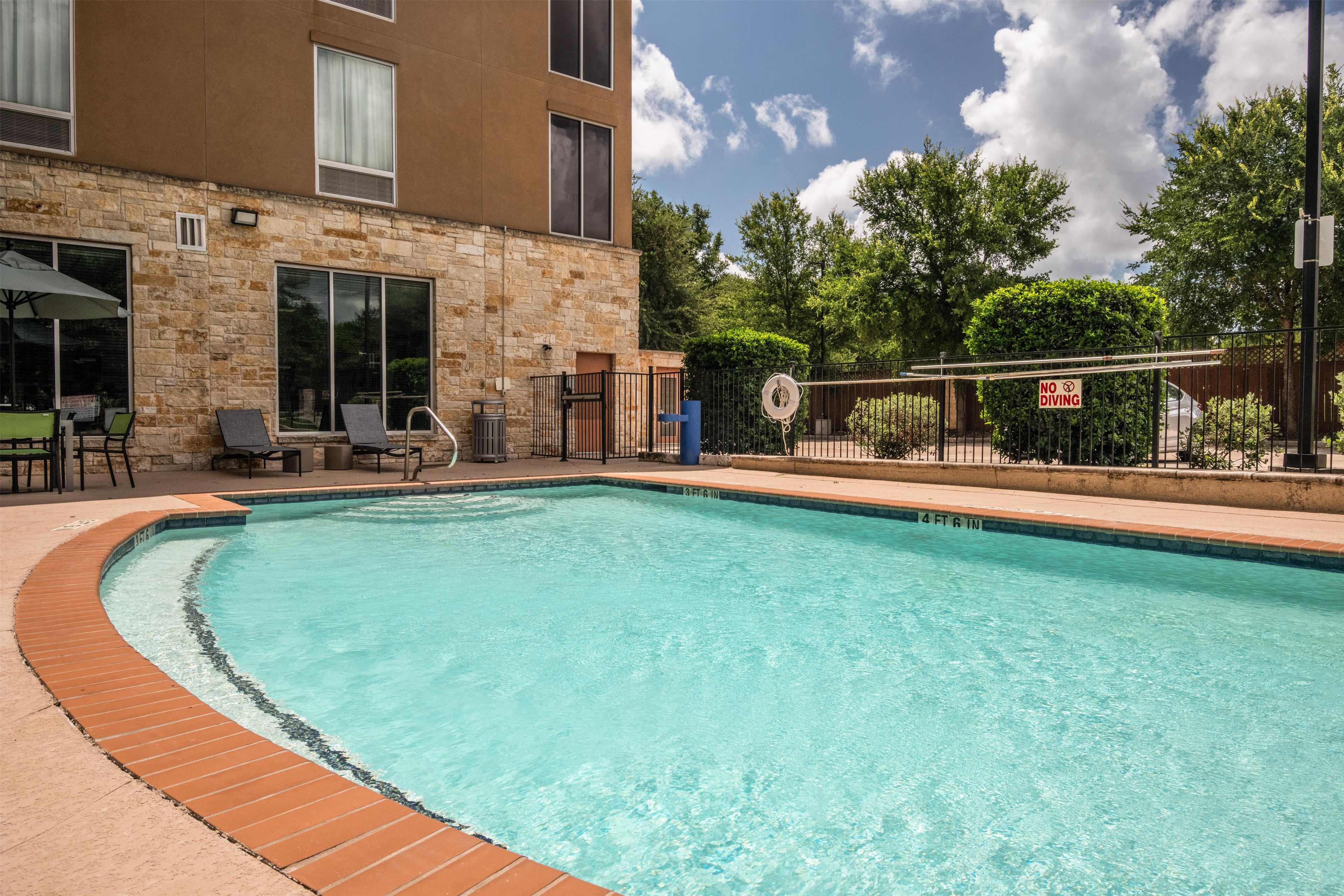 A swimming pool with a brick edge, surrounded by a stone building with windows and a door.