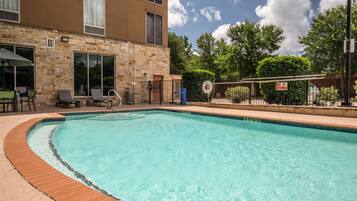 A swimming pool with a brick edge, surrounded by a stone building with windows and a door.