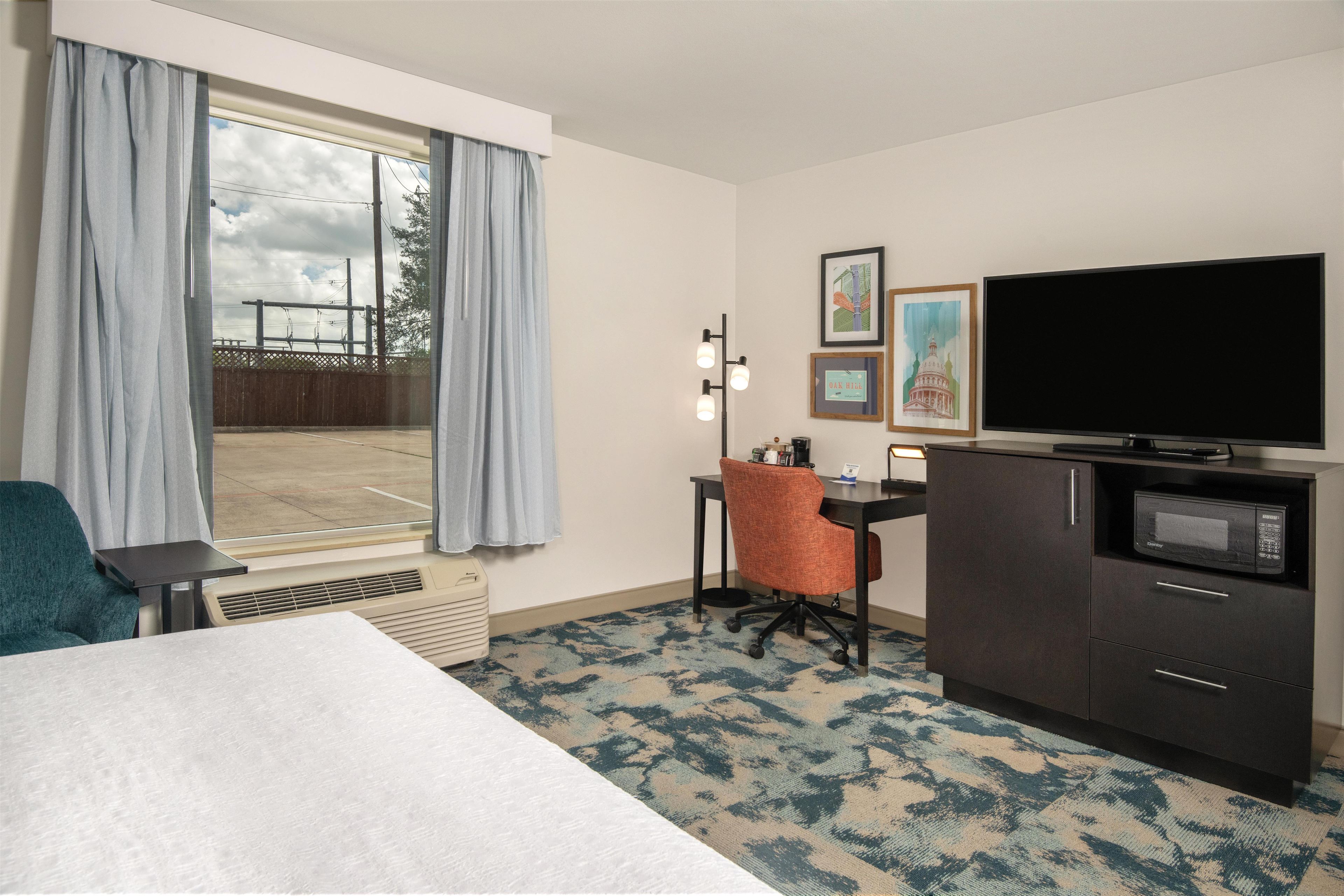 A hotel room with a bed, a desk, a chair, a television, a microwave, and a window with curtains.