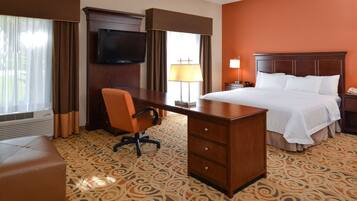 A hotel room with a bed, desk, chair, TV, and a patterned carpet.