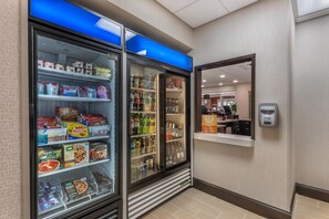 A hotel room with a minibar, a refrigerator stocked with beverages and snacks, and a small shelf with a sign. - Hampton Inn & Suites Ocala (Ocala)