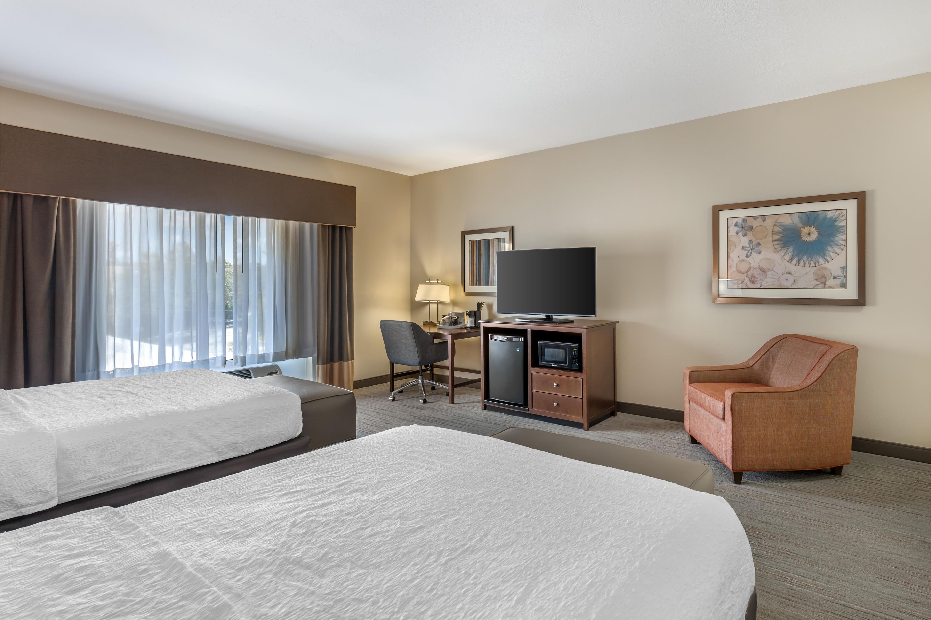 Quarto de hotel com duas camas, uma mesa de trabalho com televisão, uma cadeira e um micro-ondas.