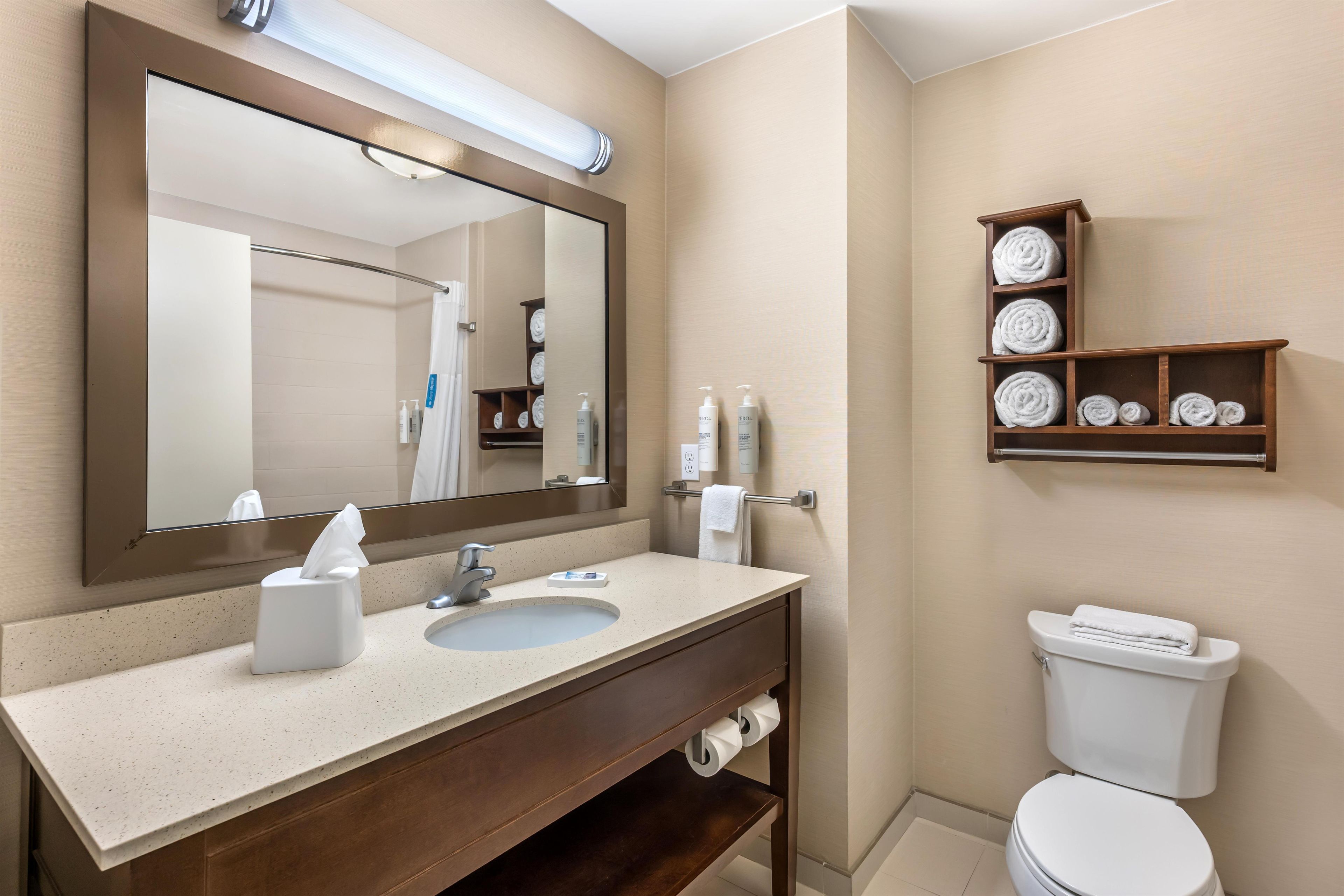 Un baño con un espejo grande, un lavabo, un inodoro y un estante con toallas.
