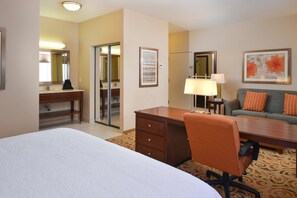 Quarto de hotel com cama, escrivaninha, poltrona, sofá, luminária e espelho.