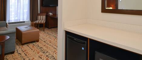 Une chambre d’hôtel équipée d’un canapé, d’un pouf, d’un téléviseur à écran plat fixé au mur, d’un four à micro-ondes et d’un réfrigérateur.