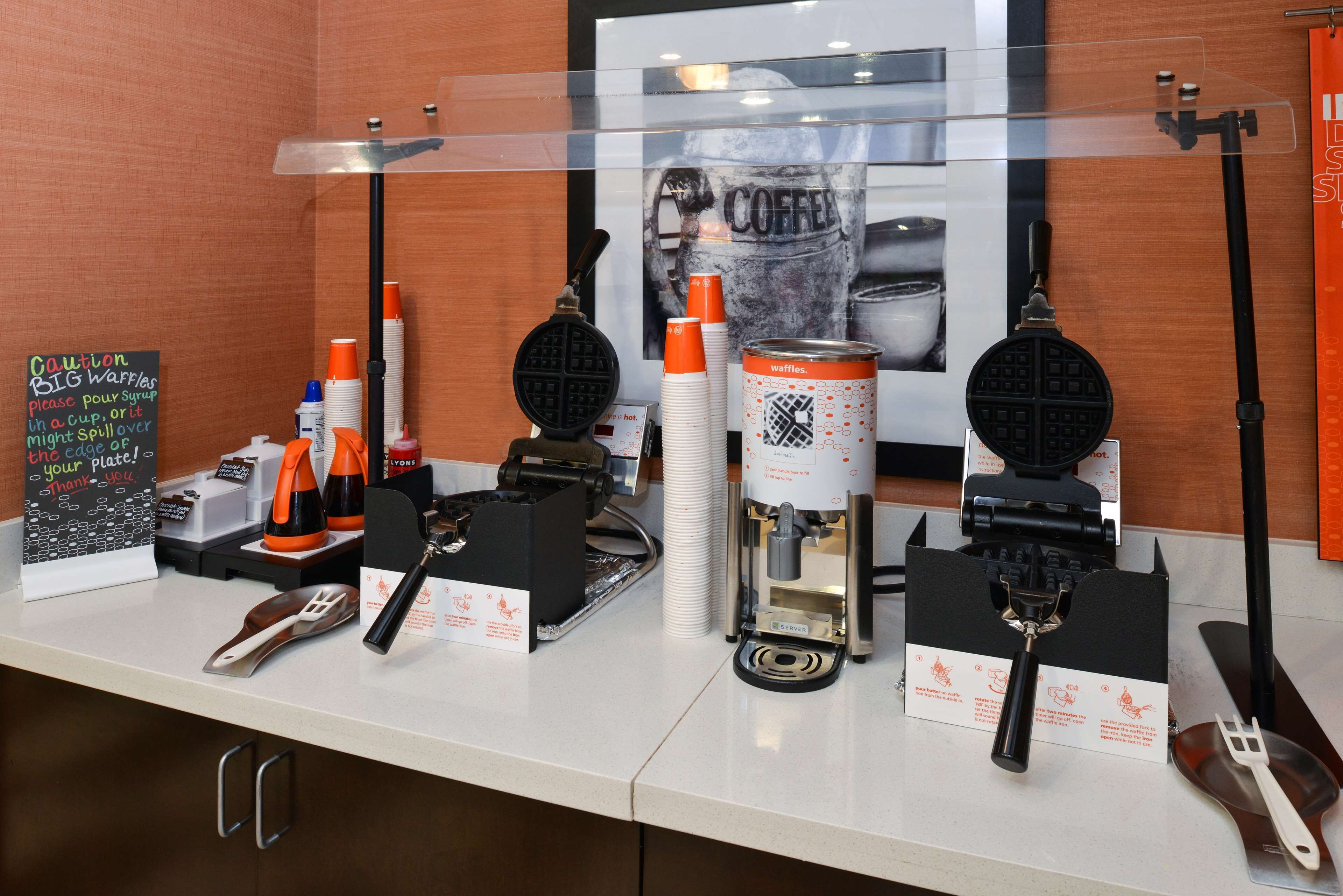 A waffle station with waffle makers, waffle cups, and syrup dispensers.