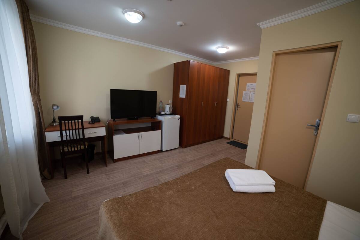 Una habitación con cama, escritorio, silla, televisor y armario.