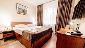 A hotel room with a wooden bed, a desk with a telephone, and a painting on the wall. - Chagala Aksai (Aksay)