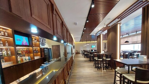 A bar area with a long counter, wooden paneling, and a television screen. There are tables and chairs in the background. - Chagala Aksai (Aksay)