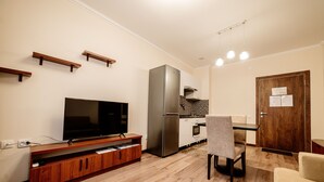 A modern kitchen with a built-in refrigerator, a flat-screen TV, wooden shelves, and a dining area with a chair. - Chagala Aksai (Aksay)