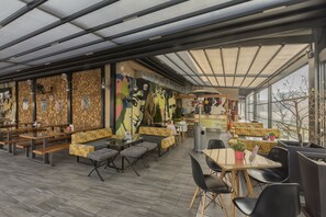 A modern restaurant with a high ceiling, glass walls, and a variety of seating options including tables, benches, and cushioned seating. - Hotel Lirak (Tetovo)